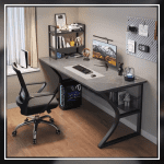 A modern gaming desk setup featuring a sleek, gray desk with a curved black frame. The desk holds a monitor displaying a mountain landscape, a keyboard, a mouse, and various accessories. A gaming PC with blue LED lights is positioned underneath. The wall has a pegboard with a digital clock and other items.