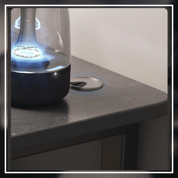 A modern gaming desk setup featuring a sleek, gray desk with a curved black frame. The desk holds a monitor displaying a mountain landscape, a keyboard, a mouse, and various accessories. A gaming PC with blue LED lights is positioned underneath. The wall has a pegboard with a digital clock and other items.