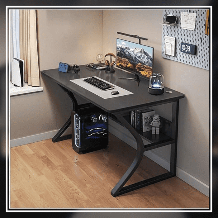 A modern gaming desk setup featuring a sleek, gray desk with a curved black frame. The desk holds a monitor displaying a mountain landscape, a keyboard, a mouse, and various accessories. A gaming PC with blue LED lights is positioned underneath. The wall has a pegboard with a digital clock and other items.